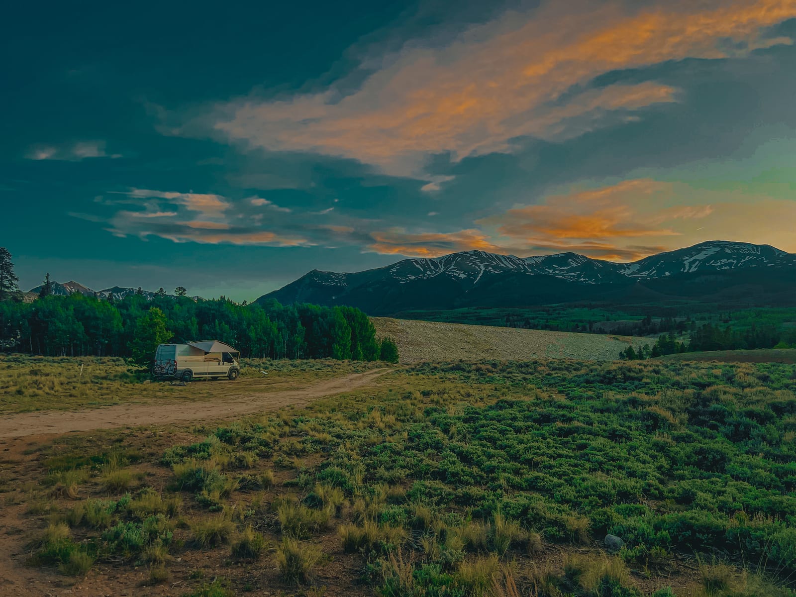 A camper van parked in a high mountain valley beneath a sunset sky, Colorado.